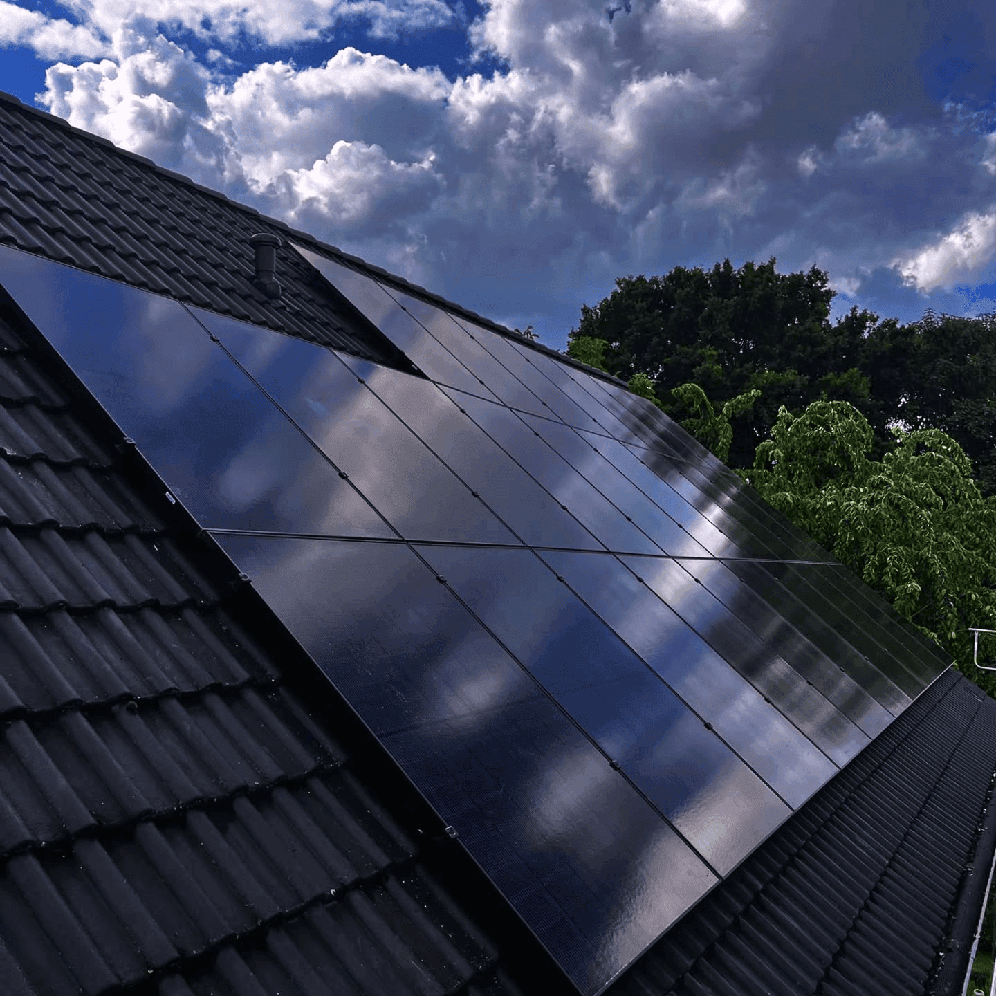 Full-Black-Photovoltaikmodule auf einem schwarzen Ziegeldach vor bewölktem Himmel